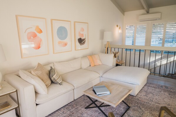 Spacious living room with plush cream couch, smart TV, and forest views. 