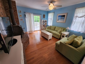 Living room w/ large screen TV, Chromecast, wood floors, cozy sofa & wide chair.