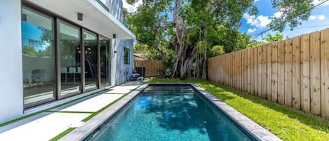 Pool right outside of double doors surrounded by beautiful grass and a big tree