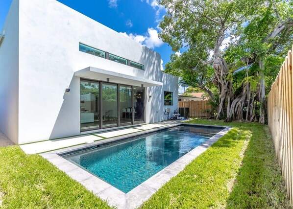 Private pool in home's backyard surrounded by grass and a tall tree for some shade