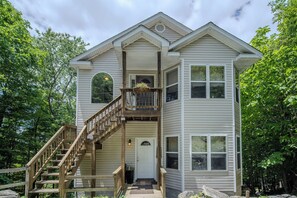 Cozy two-story home with balcony, lush greenery, and rustic charm.