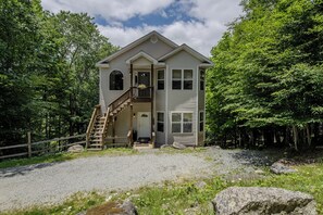Charming two-story home with large windows, outdoor area, and lush greenery.