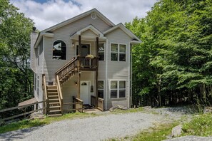 Elegant two-story home with balcony, lush greenery, and rustic charm.