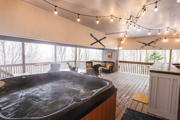 Spacious covered deck with a hot tub, cozy seating, string lights, and resort access.