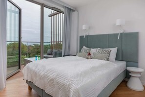 A cozy sleeping zone with white linens and a soft green headboard, surrounded by floor-to-ceiling windows.