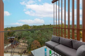 A spacious balcony with a sofa and a coffee table, providing panoramic views of greenery.