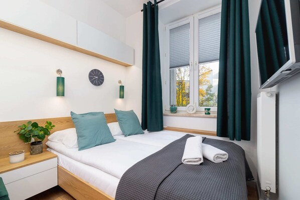 A cozy bedroom with a comfortable bed, green curtains, and wooden shelving, creating a warm and inviting atmosphere.
