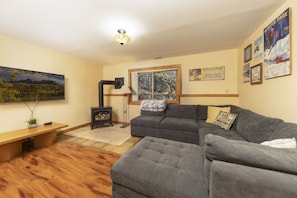 Basement level family room with gas burning wood stove and smart TV.