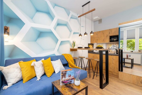 A stylish living area with a blue accent wall, honeycomb decor, a comfortable sofa, and bright yellow cushions, creating a modern and inviting space.
