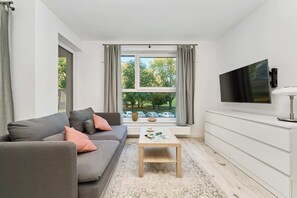 A bright living room featuring a gray sofa, modern TV stand, and a large window for natural light.
