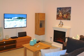 Wohnbereich mit Sofa, Sessel, Couchtisch, Elektrokamin und Sideboard mit TV