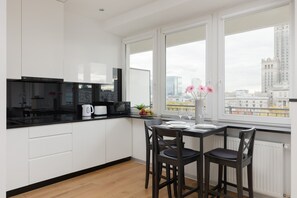 A sleek kitchen with white cabinetry, black countertops, and a dining table, blending style and functionality.
