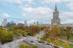 A panoramic view of the city with colorful autumn trees and iconic architecture, including the Palace of Culture and Science.
