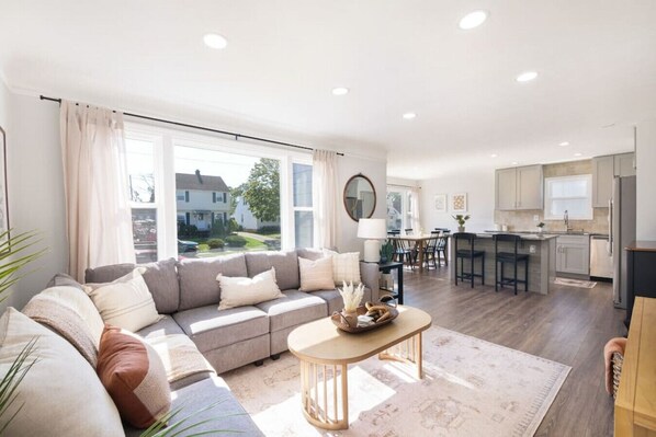 Open-plan living area bathed in natural light, anchored by a plush sectional and layered rug—effortless flow from the cozy lounge to the dining nook and kitchen beyond. 🛋️🌞