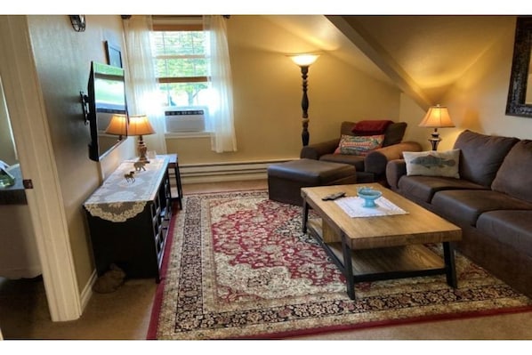 Cozy living room includes a large smart TV, air conditioner and view of park.