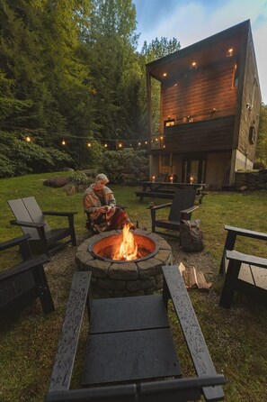 Backyard complete with fire pit, Polywood Adirondack chairs, picnic table and string lights. Enjoy the relaxing sound of the river from the backyard!