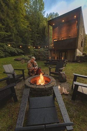 Backyard complete with fire pit, Polywood Adirondack chairs, picnic table and string lights.