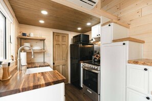 The kitchen with farmhouse sink, butcher block counter tops, full stove / oven and apartment-sized fridge + freezer.