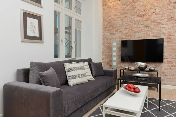 A cozy living room with a gray sofa, glass coffee table, and exposed brick wall, creating a modern yet rustic vibe.
