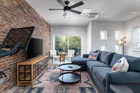 The living room captured in the image exudes a contemporary charm, defined by its clean lines and modern furnishings. Dominating the space is a plush dark grey sectional sofa, inviting relaxation with its array of patterned throw pillows. 