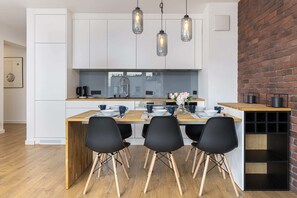 A modern kitchen with white cabinetry, a wooden island, and black chairs around the dining table.