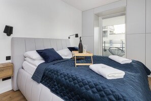 A cozy bedroom with a large double bed, white and blue bedding, and a contemporary wall art piece above the bed.