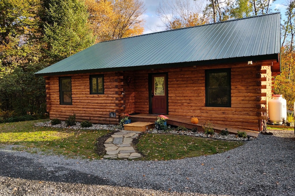 A wooden log cabin in Vermont with a stone pathway on an early autumn day