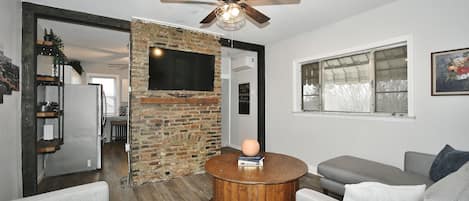 Living Room Featuring Exposed Brick, Open Layout, And A 50" Smart TV