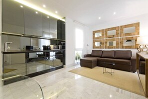 View of the living room, with a sofa,a  television and design decoration. Next to the living room is the kitchen, fully equipped with ceramic hob, toaster, coffee maker and kitchen utensils.