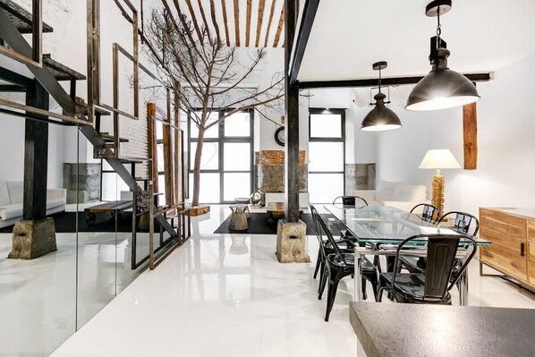 General view of the dining room  seen from the kitchen area. There is a dining table for six people and 
in the background, the entrance door and the living room area with a sofa bed.