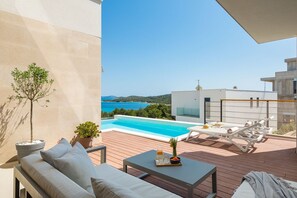 A view of the sea from the outdoor seating area on the roofed patio with pool and sunloungers of the modern vacation villa on Murter