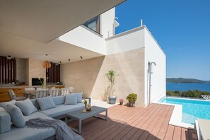 Summer kitchen with dining table and outdoor seating on the roofed patio with pool of the luxury vacation villa Villa Murter Exotic