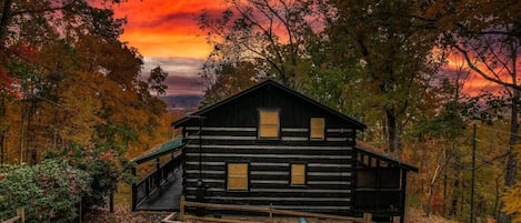 Our rustic hand-hewn log cabin stands tall amidst a tranquil forest in Pigeon Forge. The warm glow of the setting sun casts a golden hue on the cabin's walls, inviting you to cozy up inside for the night.