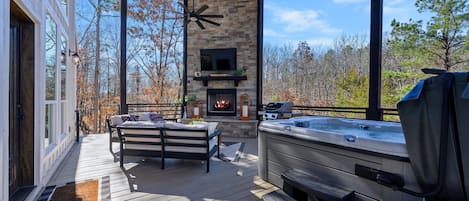 Outdoor covered deck with seating, fireplace, TV, and hot tub