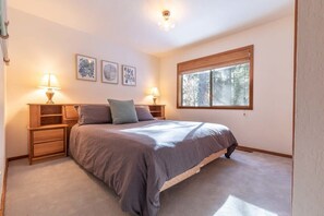 The first of three bedrooms downstairs features a king-size bed, two nightstands with lamps, a large window, and extra storage space for your items by the bed.