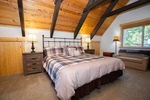 The master bedroom boasts a king-size bed, matching nightstands with lamps, a comfortable sofa underneath the window, a large dresser with a 32” TV on top, and an ensuite bathroom.