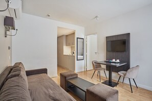 Expanding into the main living area, you'll discover a comfortable sofa set, a dining space for two, and a mounted TV, creating an ideal setup for relaxation and entertainment in your Paris retreat.