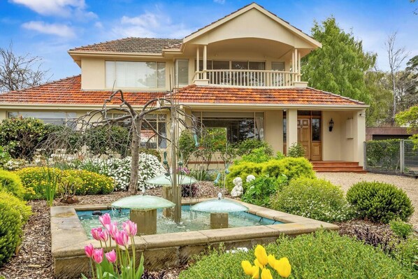 Beyond the gate, the front yard welcomes you with a circular driveway and a lush garden with a fountain.