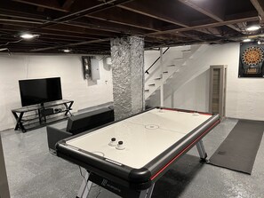 Basement with a 55 inch smart tv, air hockey and a dart board.