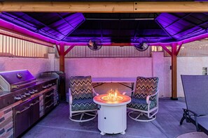 Cozy outdoor space with a fire pit, BBQ grill, and vibrant lighting—perfect for relaxing evenings