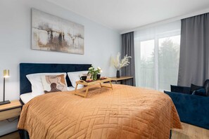 A bedroom with a warm orange duvet and modern decor, including a wall-mounted painting.

