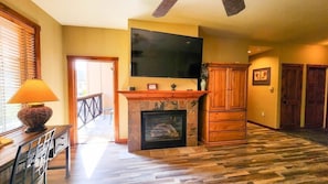 The view from the living room sofa highlights key features of the space;  a gas fireplace, large flatscreen tv,  desk looking out the windows, and access to the private balcony.