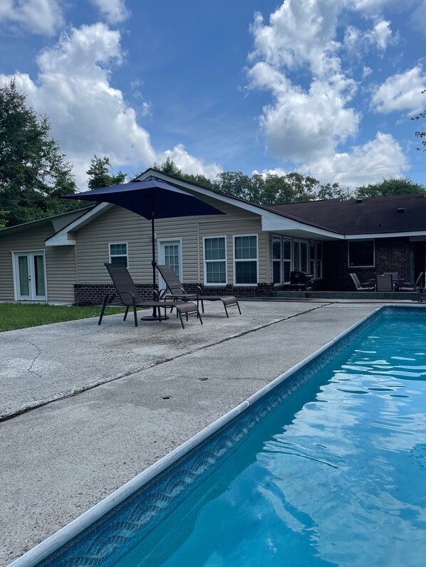 Deep end of pool area viewing the outdoor patio, back of house and back yard.