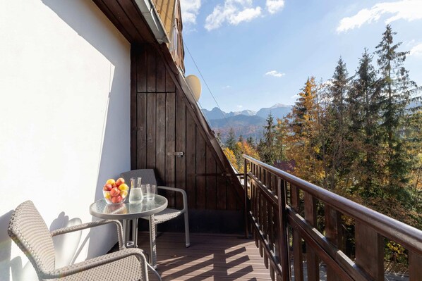A charming balcony with a small table and chairs overlooking a forested mountain view.
