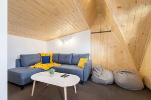 A cozy living room with wooden paneling, a blue sectional sofa, and yellow accents.
