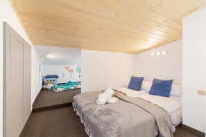 A bedroom with a sloped wooden ceiling, featuring a neatly made bed and soft lighting.
