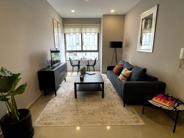 
Enter the living room flooded with natural light, featuring a comfortable couch, a TV, and a coffee table. By the window, a small table awaits for dining or work, accommodating two. Enjoy the serene atmosphere and scenic view.
