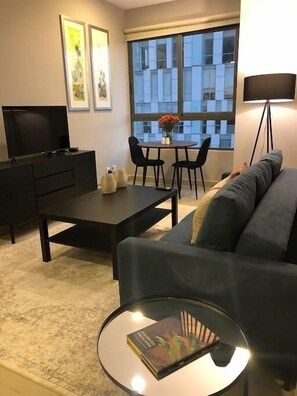 Living roomStep into the well-lit living room, boasting a cozy couch, a TV, and a coffee table. By the window, a small table provides a perfect spot for dining or working, accommodating two. Whether day or night, savor the serene ambiance and take in the captivating view.