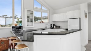 Fully equipped kitchen looks pristine, with its white cabinets contrasting with the black countertops and an island benchtop