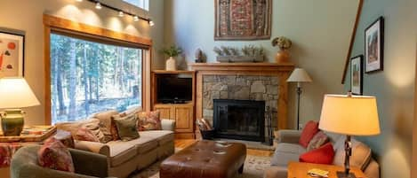 This charming home's bright and open living room features high ceilings and spacious windows perfect for watching the snowfall or enjoying the nature views as you relax by the fire.